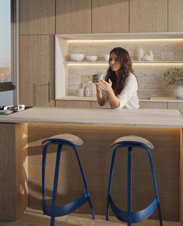 סגנון חיים – אישה במטבח עם כוס קפה, כסאות בר ותאורה חמה